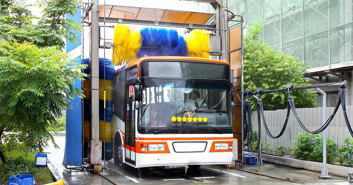 A bus is being washed with rotating brushes at an automated vehicle wash station.