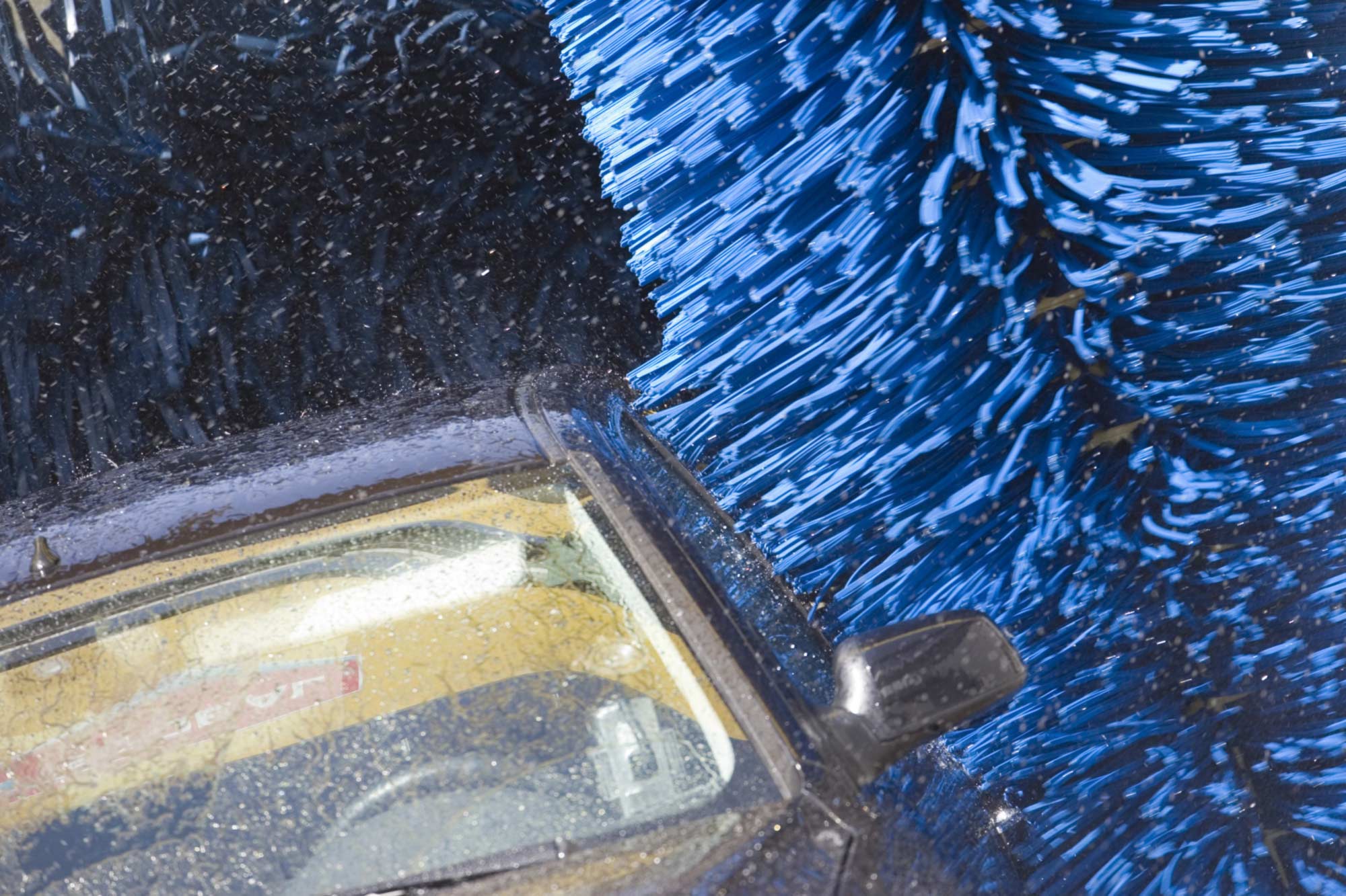 A car is going through an automatic car wash with blue brushes cleaning its surface.