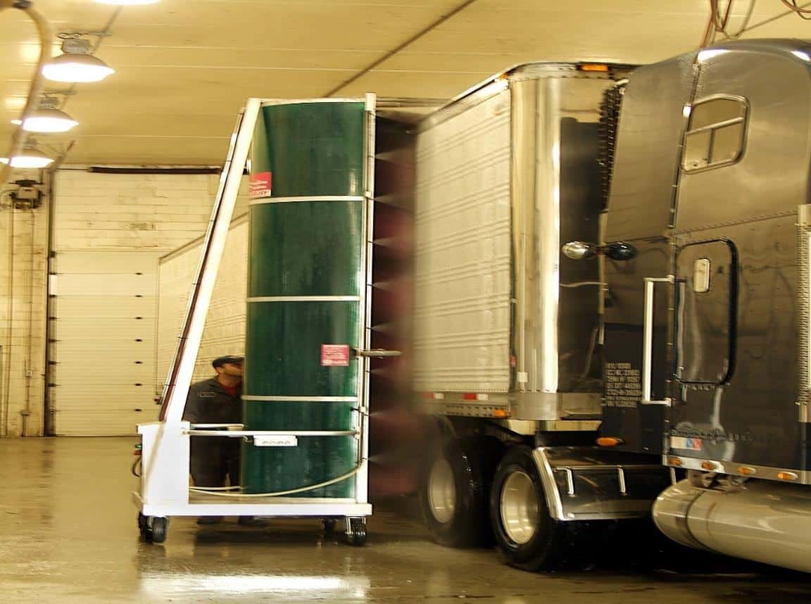 A large freight truck with its trailer doors open, revealing a tall industrial rolling cart being moved by a person inside a warehouse.