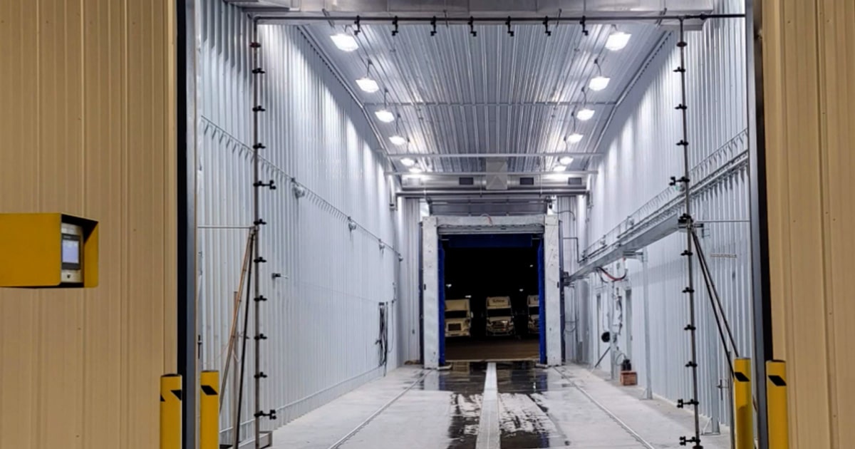 A brightly lit industrial hallway leading to a warehouse area with visible cargo and loading docks.