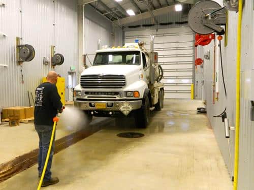 A person is pressure washing a white truck inside an industrial cleaning bay.
