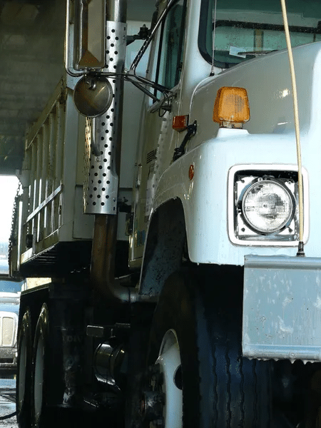 A close-up of a white semi-truck's front end, showcasing the headlight, grille, and side mirror assembly.