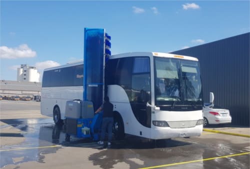 A white bus is being washed at an outdoor cleaning station under clear skies.