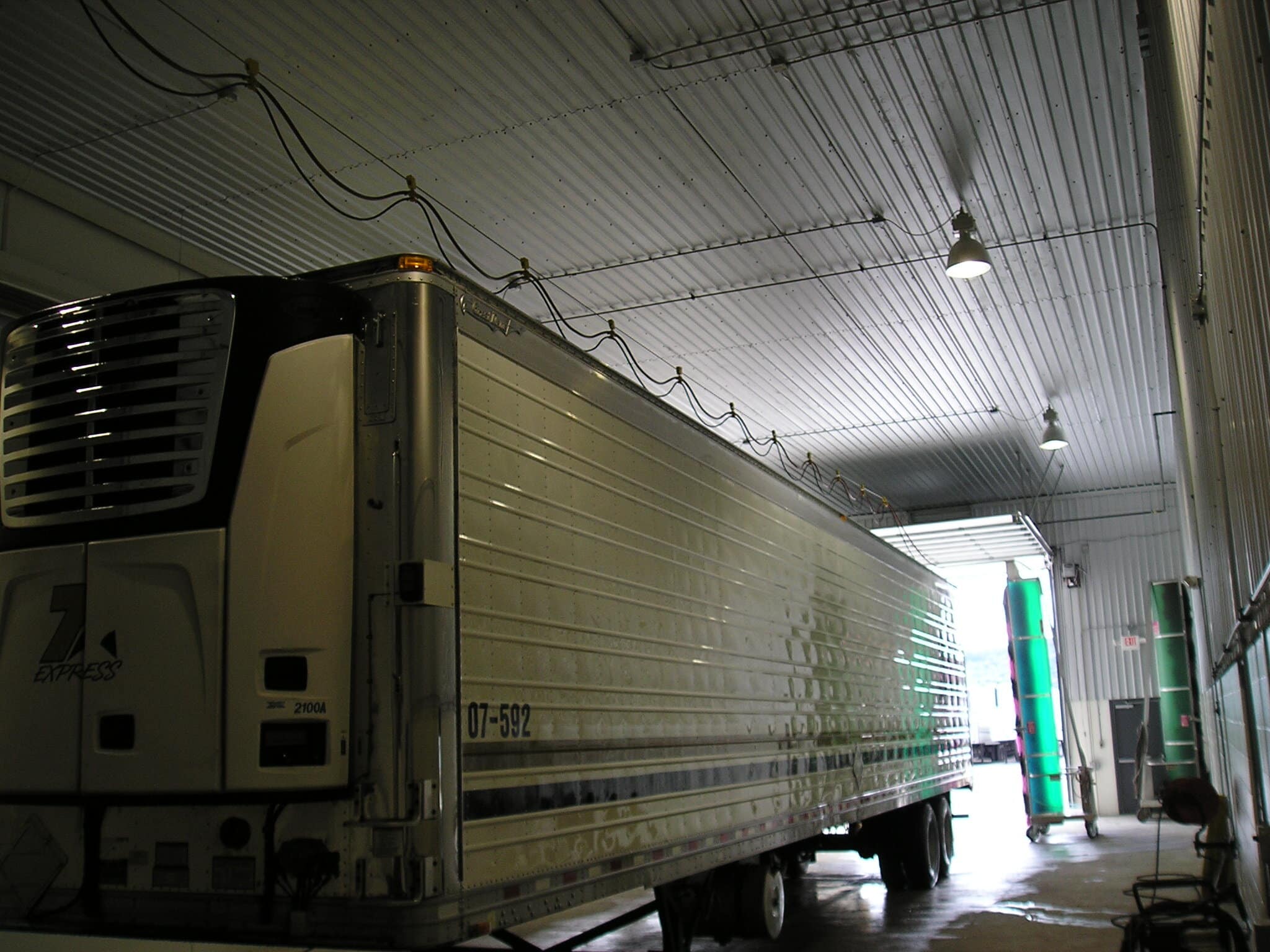 A semi-truck parked inside a spacious industrial warehouse with overhead lighting and visible electrical conduits.