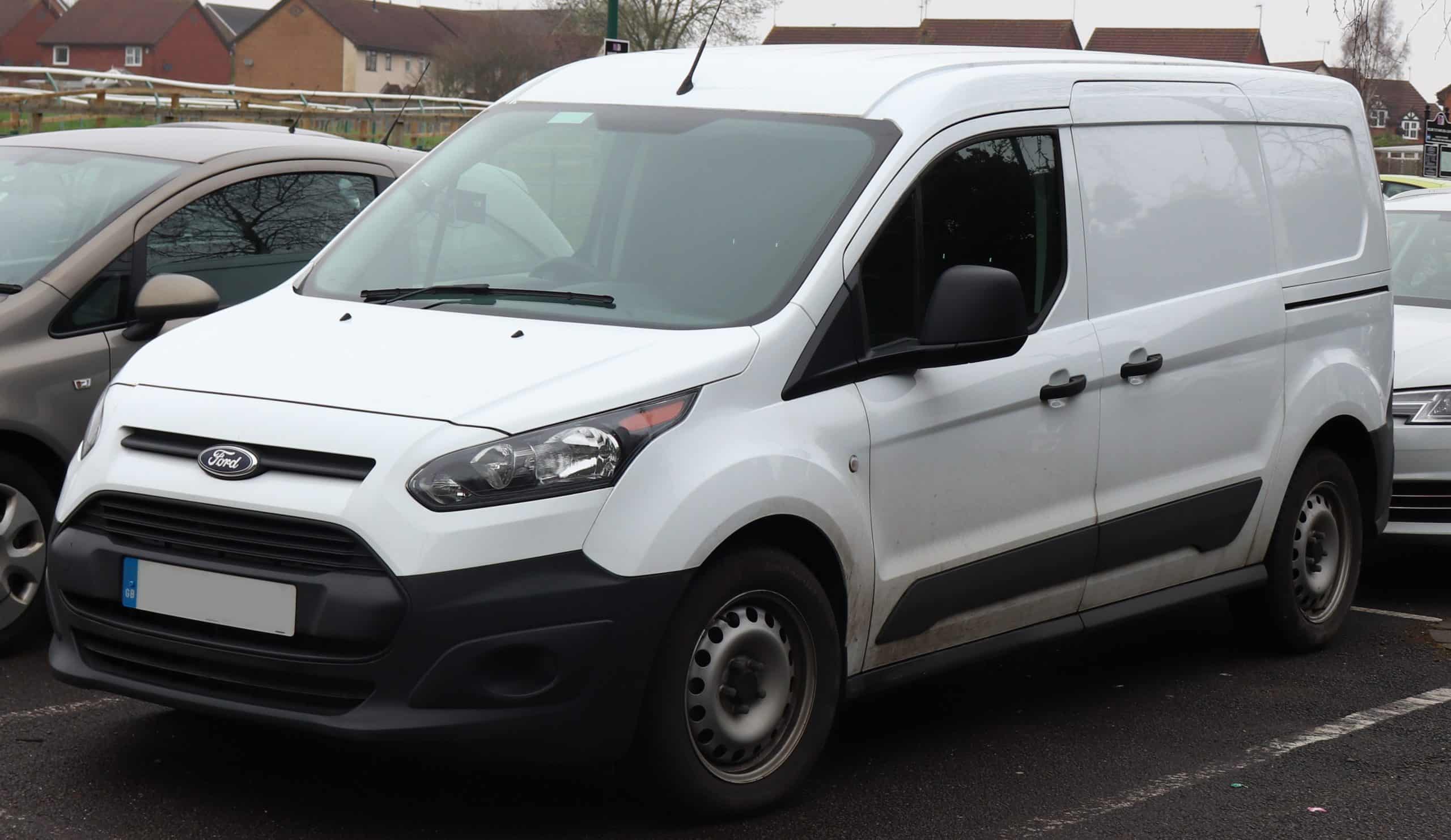 A white Ford Transit Connect van parked in a parking lot with other vehicles in the background.