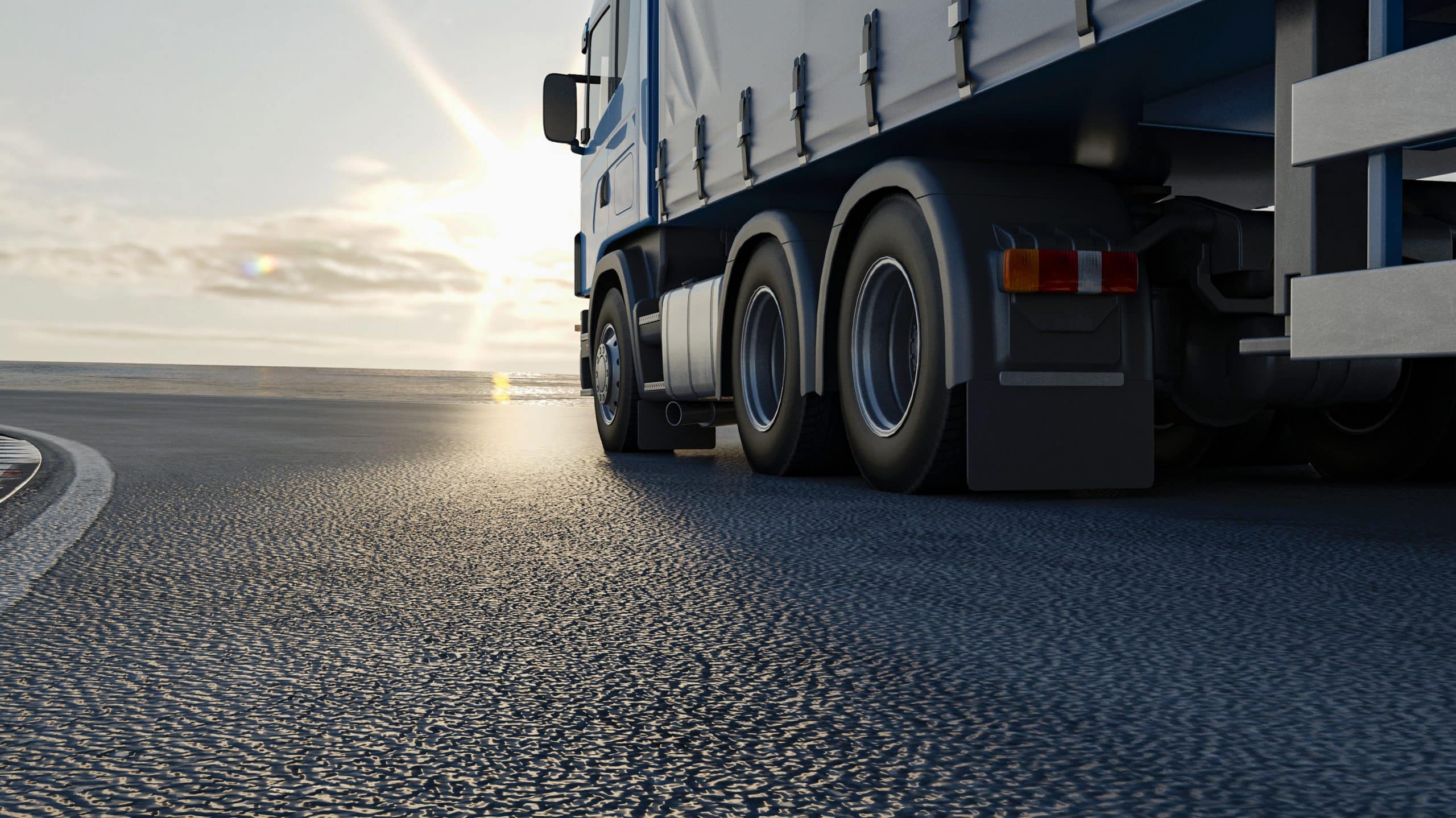 A close-up view of a semi-truck traveling on a highway at sunset, emphasizing the wheels and side of the trailer.