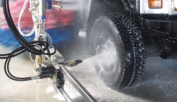 An automated car wash system is cleaning a vehicle's tire with high-pressure water jets.